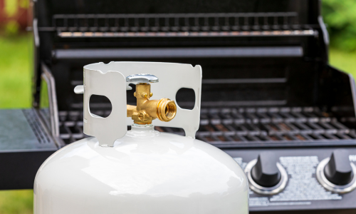 A propane tank sitting in front of a grill